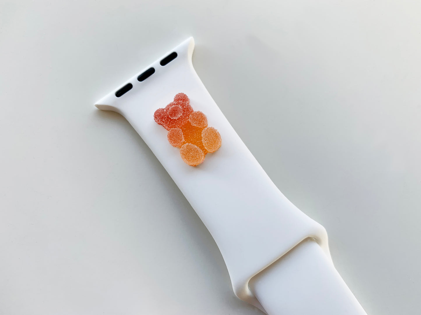 A small red and orange 3D printed gummy bear attached to a white silicon watch strap for the apple watch