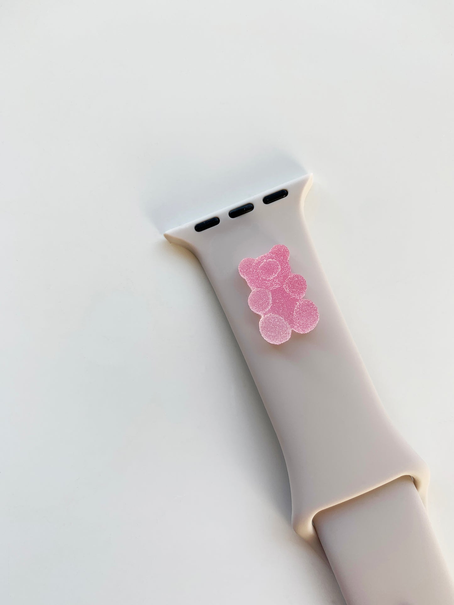 A small pink 3D printed gummy bear attached to a starlight silicon watch band for the apple watch
