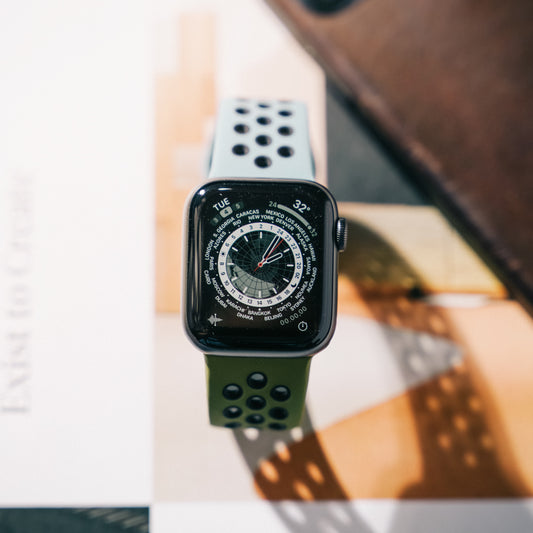 A grey sports active watch strap on an apple watch with a compass watch face on a desk