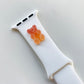 A small red and orange 3D printed gummy bear attached to a white silicon watch strap for the apple watch